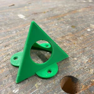 May include: A green plastic triangle with a round hole in the center and two rounded protrusions on the bottom.