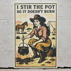 May include: A vintage-style print featuring a cowgirl stirring a pot over a campfire. The image includes a horse, a tent, and the text "I STIR THE POT SO IT DOESN'T BURN." The color palette is primarily beige, brown, and peach.