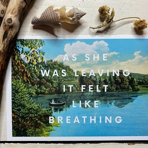 May include: A rectangular postcard featuring a vintage-style landscape illustration of a lake with a small canoe and lush green trees under a blue sky. The white text overlay reads: AS SHE WAS LEAVING IT FELT LIKE BREATHING. The print is displayed on a white surface.