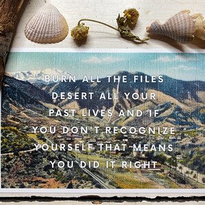 May include: A vintage postcard with a scenic mountain landscape. The postcard features the text "BURN ALL THE FILES DESERT ALL YOUR PAST LIVES AND IF YOU DON'T RECOGNIZE YOURSELF THAT MEANS YOU DID IT RIGHT."
