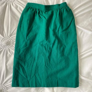 May include: A green knee-length skirt made of a textured fabric. The skirt has a simple design with a waistband and a straight silhouette.