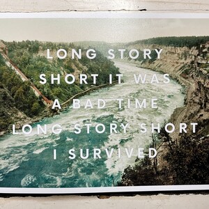 May include: A rectangular print featuring a vintage-style landscape of a river flowing through a deep canyon with steep, tree-lined cliffs. Overlaid in white sans-serif text is the phrase: LONG STORY SHORT IT WAS A BAD TIME LONG STORY SHORT I SURVIVED.