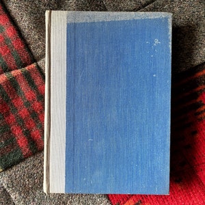 May include: A blue hardcover book with a white spine. The book is lying on a patterned fabric.