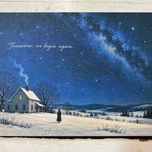 May include: A rectangular print featuring a snowy landscape at night under a starry sky with the Milky Way. A small house with a glowing window and a chimney emitting smoke sits near a lone figure. The text reads, Tomorrow, we begin again.