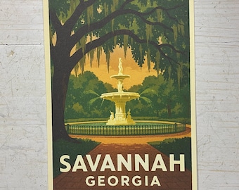 May include: A rectangular print featuring a stylized illustration of a tiered fountain in Savannah, Georgia. The scene includes a large tree with hanging moss, a brick walkway, and a fence. The text SAVANNAH GEORGIA is printed in white at the bottom.