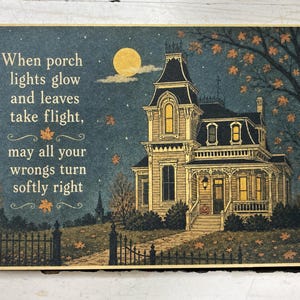 May include: A rectangular print featuring a Victorian house at night under a full moon. The text reads: When porch lights glow and leaves take flight, may all your wrongs turn softly right. Orange leaves fall around the house and a dark fence.
