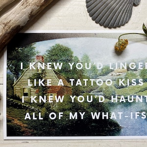May include: A vintage postcard with a painting of a house and trees. The text on the postcard reads: "I knew you'd linger like a tattoo kiss I knew you'd haunt all of my what-ifs."