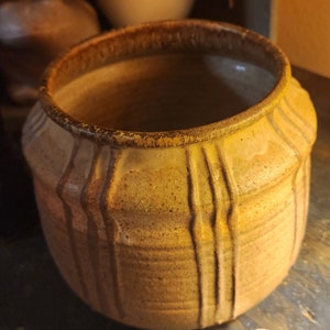 May include: A brown ceramic pot with vertical lines and a textured surface. The pot is empty and has a wide opening.