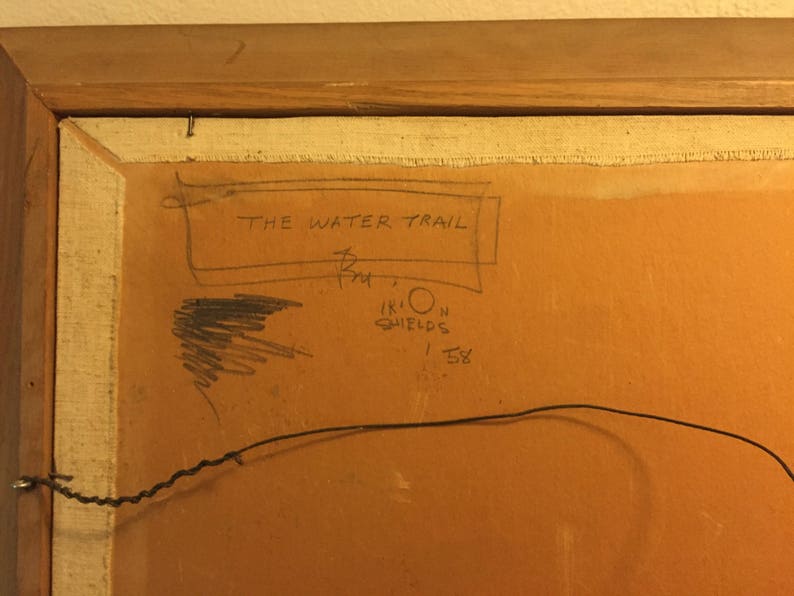 May include: A close-up of the back of a framed painting. The title "THE WATER TRAIL" is written in black ink on a white background. The artist's name, "IRION SHIELDS", and the year "1958" are also written in black ink.