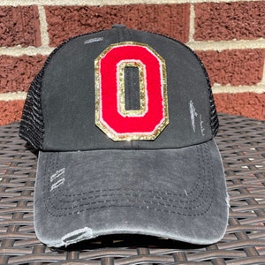 May include: Black distressed trucker hat with a red and gold felt letter 'O' on the front.
