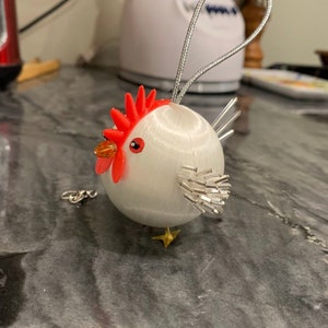 May include: White ceramic chicken ornament with red comb and wattle, gold feet, and silver glitter tail feathers.
