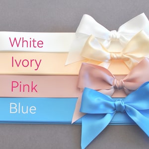 K&ouml;nnte beinhalten: Vier horizontale Satinb&auml;nder in Wei&szlig;, Elfenbein, Rosa und Blau, jeweils mit einer passenden Schleife auf der rechten Seite. Der Text White, Ivory, Pink und Blue ist in Rosa und Wei&szlig; auf der linken Seite des jeweiligen Bandes aufgedruckt.