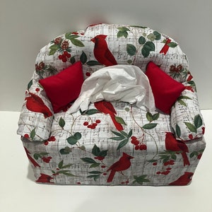 May include: A red cardinal themed tissue box cover shaped like a couch with red pillows. The fabric has a white background with musical notes, red cardinals, green leaves, and red berries.