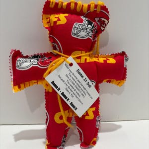 May include: A handmade red and yellow doll with the text "Damn It Doll" on a tag. The doll is made of fabric with a football helmet and team logo pattern. The doll has arms and legs and is designed to be slammed.