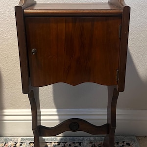 May include: A dark brown wooden side table with a single door and a handle on the top. The table has a curved, ornate base and a single drawer.