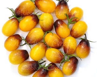 Könnte beinhalten: Eine Ansammlung gelber und brauner Tomaten mit grünen Stielen. Die Tomaten sind oval geformt und weisen einen Farbverlauf von Gelb nach Braun auf. Die Tomaten sind auf einer weißen Oberfläche angeordnet.