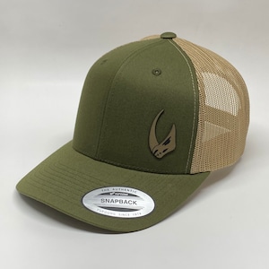 May include: A green and tan trucker hat with a brown rhinoceros logo. The hat has a mesh back and a snap closure. The hat has a label that says "The Authentic Yupoong Snapback Yupoong Since 1974".