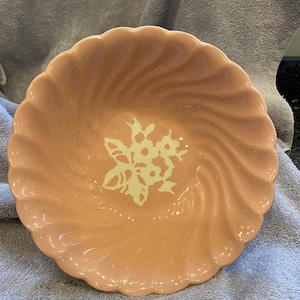 Pode incluir: Uma tigela de cerâmica rosa com um desenho floral branco. A tigela tem uma borda festonada e um design ondulado.
