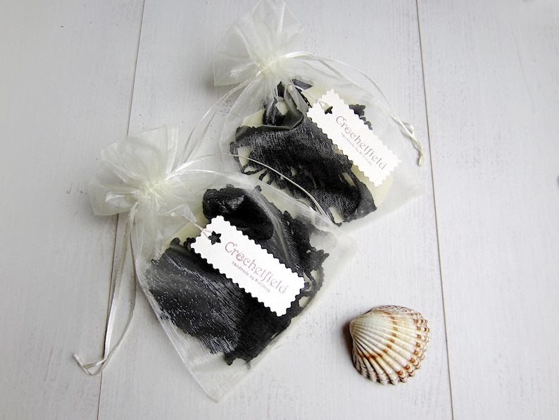 May include: Two small bags of black lace trim with white tags that say "Crechelfielf Handmade in France". The bags are made of sheer white fabric and are sitting on a white wooden surface. A small white seashell is also in the image.