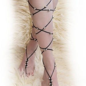 May include: Black ankle-length leg jewelry with silver beads. The jewelry is made of string and is tied around the legs and feet.