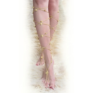 Könnte beinhalten: Goldene Häkel-Fußschmuck mit dekorativen Perlen. Der Schmuck wird an beiden Beinen getragen und wickelt sich um die Knöchel und Füße.