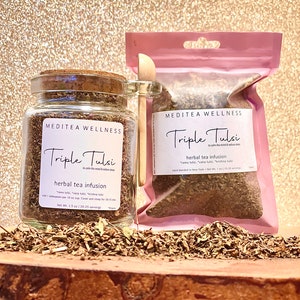 May include: A jar and a pink pouch of Triple Tulsi herbal tea infusion. The jar has a cork lid and a label with the text "MEDITEA WELLNESS" and "Triple Tulsi". The pouch also has the same text. A wooden spoon rests on the side.