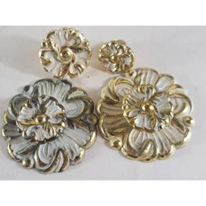 May include: A collection of decorative floral embellishments in various sizes. The pieces feature a white base with gold-colored accents, showcasing intricate details. The set includes two large and two small floral designs.