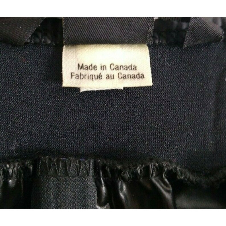 May include: Close-up of a tag that reads "Made in Canada" and "Fabriqu&eacute; au Canada" in white text. The tag is attached to a dark blue fabric. The bottom of the image shows a black, shiny, gathered material.