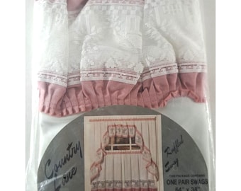 May include: A pair of pink and white ruffled swag curtains with a lace trim. The curtains are packaged in plastic and labeled "Country Love" and "Ruffled Swag". The package contains one pair of swags that are 64 inches by 38 inches.
