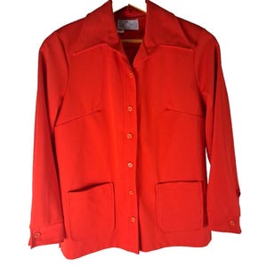May include: A bright red button-up jacket with long sleeves and two large pockets. The jacket has a collar and a button closure.