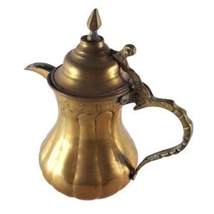 May include: A gold-coloured brass teapot with a decorative handle and a lid with a pointed finial. The teapot has a bulbous body with vertical ridges.