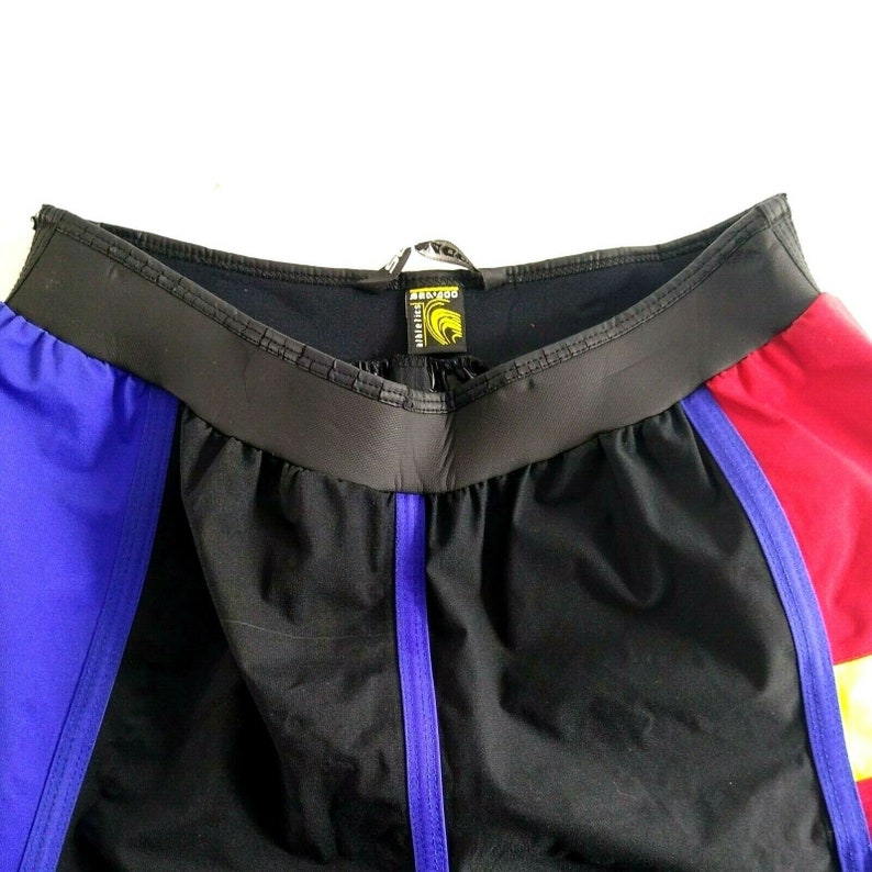 May include: Black athletic shorts with panels of red and blue. The shorts have a black waistband and a purple stripe down the front. The tag reads "Athletics".