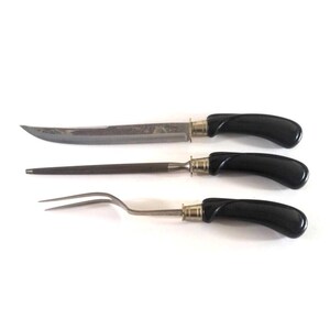 May include: A set of three vintage kitchen utensils with black plastic handles. The set includes a carving knife, a steak knife, and a fork.