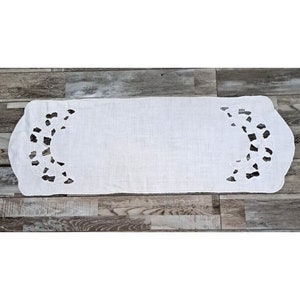 Può includere: Un runner da tavolo bianco con un delicato motivo di pizzo floreale su ogni estremità. Il runner è realizzato in un tessuto morbido e leggero, perfetto per aggiungere un tocco di eleganza a qualsiasi mise en place.