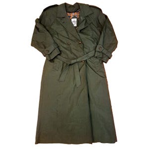 Könnte beinhalten: Olivgrüner Trenchcoat mit doppelreihiger Knopfleiste, Taillengürtel und geknöpften Manschetten. Der Mantel hat ein klassisches Design mit einem Kragen und einer langen Länge. Das Innenfutter hat ein Muster.