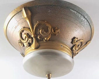 Puede incluir: Una lámpara de techo vintage con acabado dorado y detalles ornamentados. La luz tiene una pantalla de vidrio esmerilado y un ribete metálico decorativo.