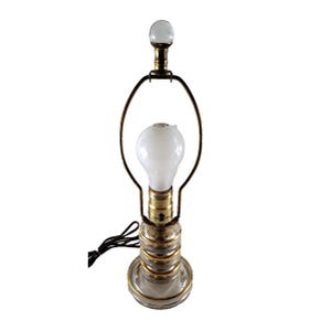May include: A clear glass table lamp with brass accents and a white light bulb. The lamp has a round base and a decorative brass ring around the middle. The lamp is approximately 12 inches tall.