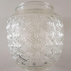 May include: Clear glass jar with a decorative pattern of swirling lines and small circles. The jar has a wide, rounded body and a slightly narrower opening at the top. The glass is transparent, allowing light to pass through.