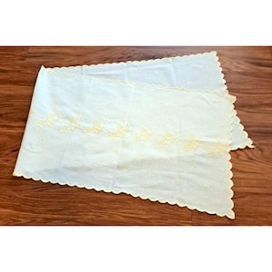 May include: A white table runner with a scalloped edge and embroidered yellow butterflies.