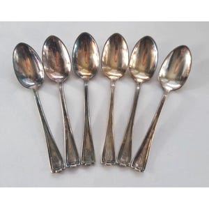 以下が含まれることがあります： 装飾的なハンドルが付いた銀製のティースプーン6本セット。スプーンは一列に並んでおり、ハンドルは視聴者の方向を向いています。