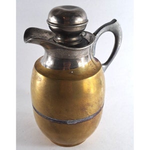 May include: A vintage silver and brass pitcher with a lid. The pitcher has a rounded body and a silver spout. The lid is also silver and has a rounded top.