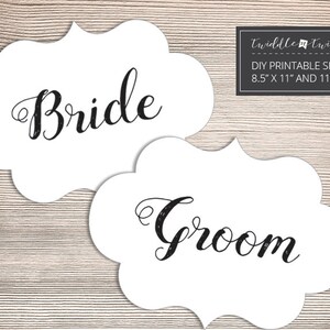 May include: Two printable signs with a white background and black calligraphy text. The signs are shaped like a cloud with scalloped edges. The text on the signs reads "Bride" and "Groom". The signs are 8.5 inches by 11 inches and 11 inches by 14 inches.