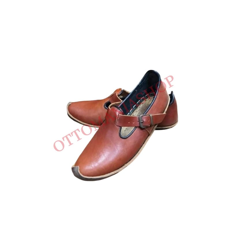 Puede incluir: Un par de zapatos de cuero marr&oacute;n con una hebilla. Los zapatos tienen una punta puntiaguda y un tac&oacute;n bajo.