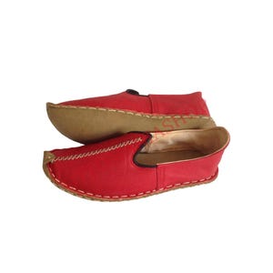 May include: A pair of red leather slip-on shoes with a brown sole and white stitching.