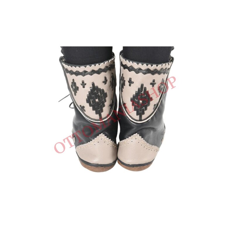 May include: Black leather ankle boots with a beige toe and heel. The boots have a geometric pattern embroidered on the back of the boot.