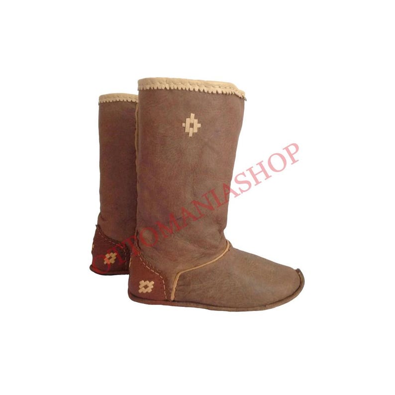 K&ouml;nnte beinhalten: Ein Paar braune Lederstiefel mit cremefarbenem Besatz und Stickereien. Die Stiefel haben eine abgerundete Spitze und eine flache Sohle.