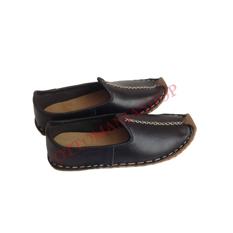 May include: A pair of black leather slip-on shoes with a pointed toe and a stitched seam around the edge. The shoes have a brown leather trim around the toe.