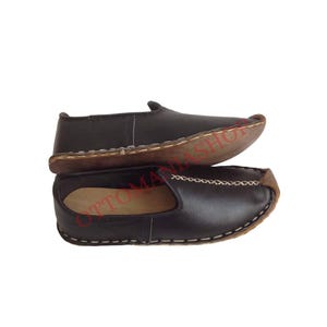 May include: A pair of black leather slip-on shoes with a brown leather sole and white stitching. The shoes are made of soft leather and have a comfortable fit.