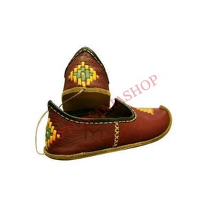 May include: A pair of red leather shoes with yellow and green embroidered designs. The shoes have a pointed toe and a flat sole.