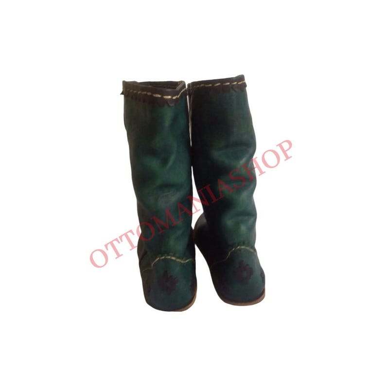 K&ouml;nnte beinhalten: Ein Paar gr&uuml;ne Lederstiefel mit schwarzen N&auml;hten und einem dekorativen Design. Die Stiefel sind hoch und haben eine spitze Zehenpartie.